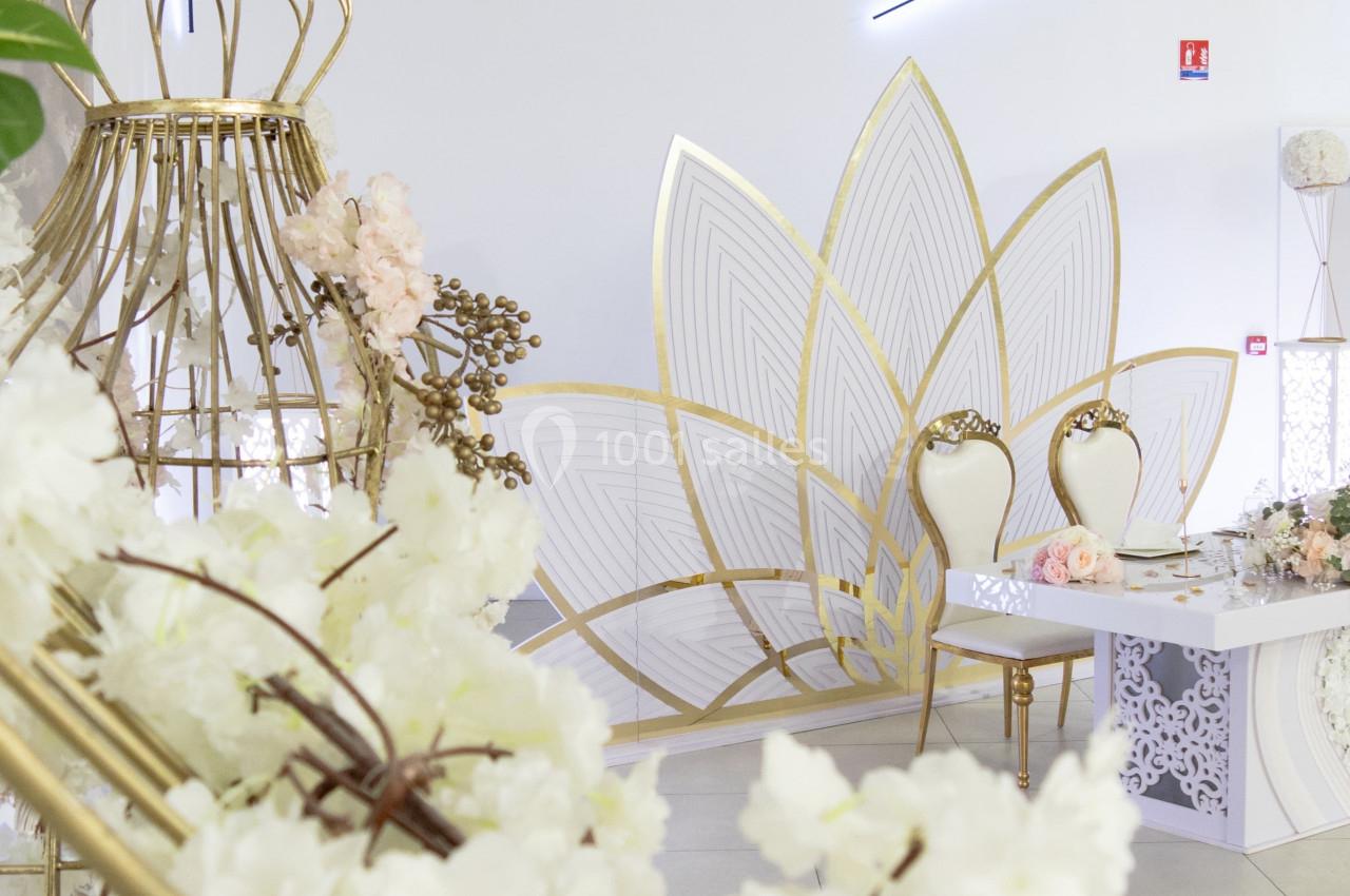 Décoration de salle avec fleurs blanches, chaises élégantes et structures dorées dans un espace lumineux.