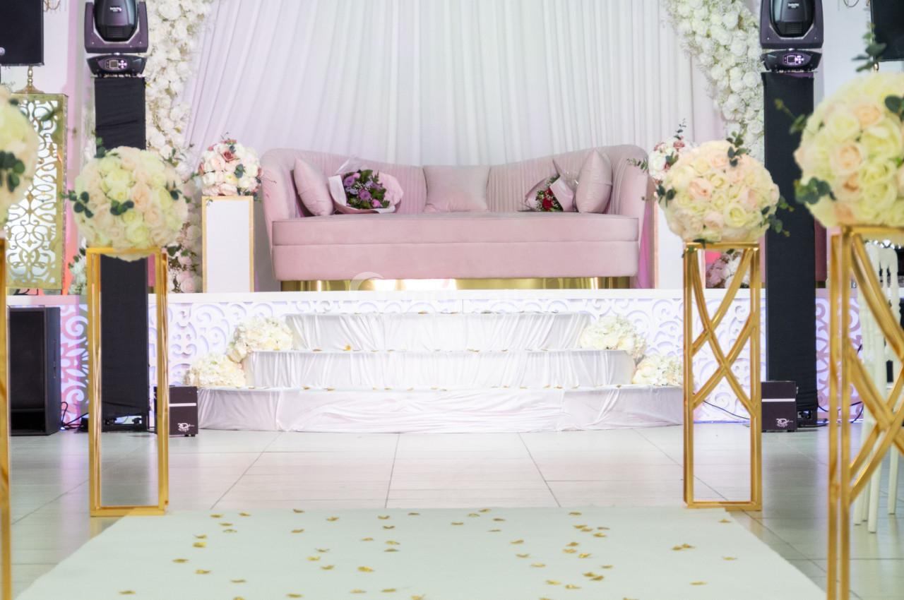 Salle de réception décorée avec un canapé rose, des fleurs blanches et roses, et une allée parsemée de pétales.