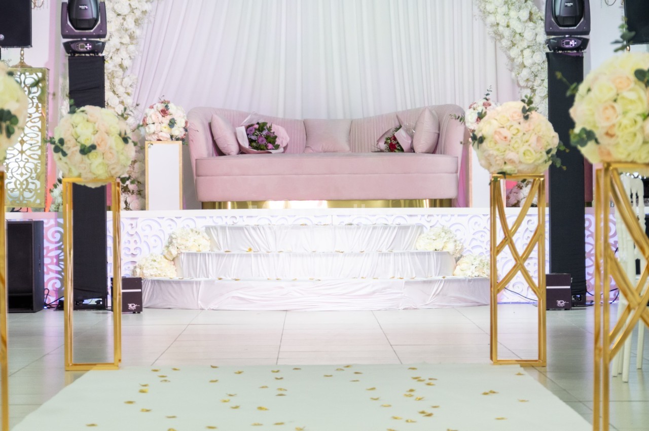 Salle de réception décorée avec un canapé rose, des fleurs blanches et roses, et une allée parsemée de pétales.