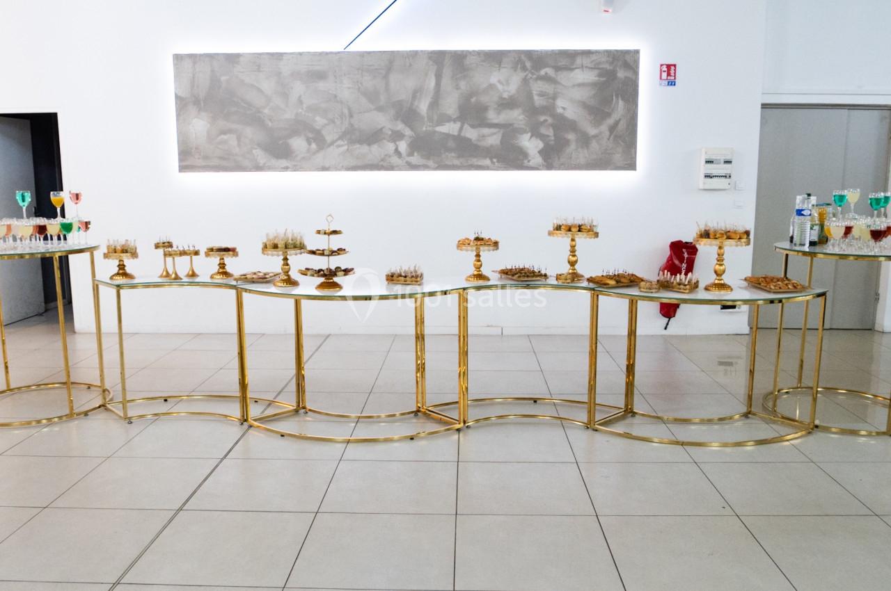 Buffet élégant avec desserts variés présentés sur des plateaux dorés dans une salle lumineuse au décor minimaliste.