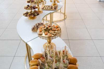 Miniature Location salle Brétigny-sur-Orge (Essonne) - Aya Réception #36 Buffet élégant avec une présentation variée de bouchées salées et sucrées sur des plateaux dorés en salle lumineuse.