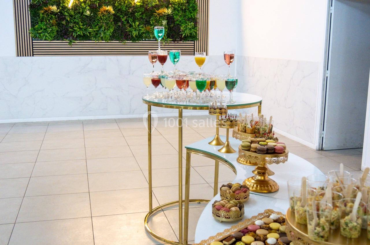 Buffet élégant avec desserts variés, cocktails colorés et mur végétal éclairé en arrière-plan.