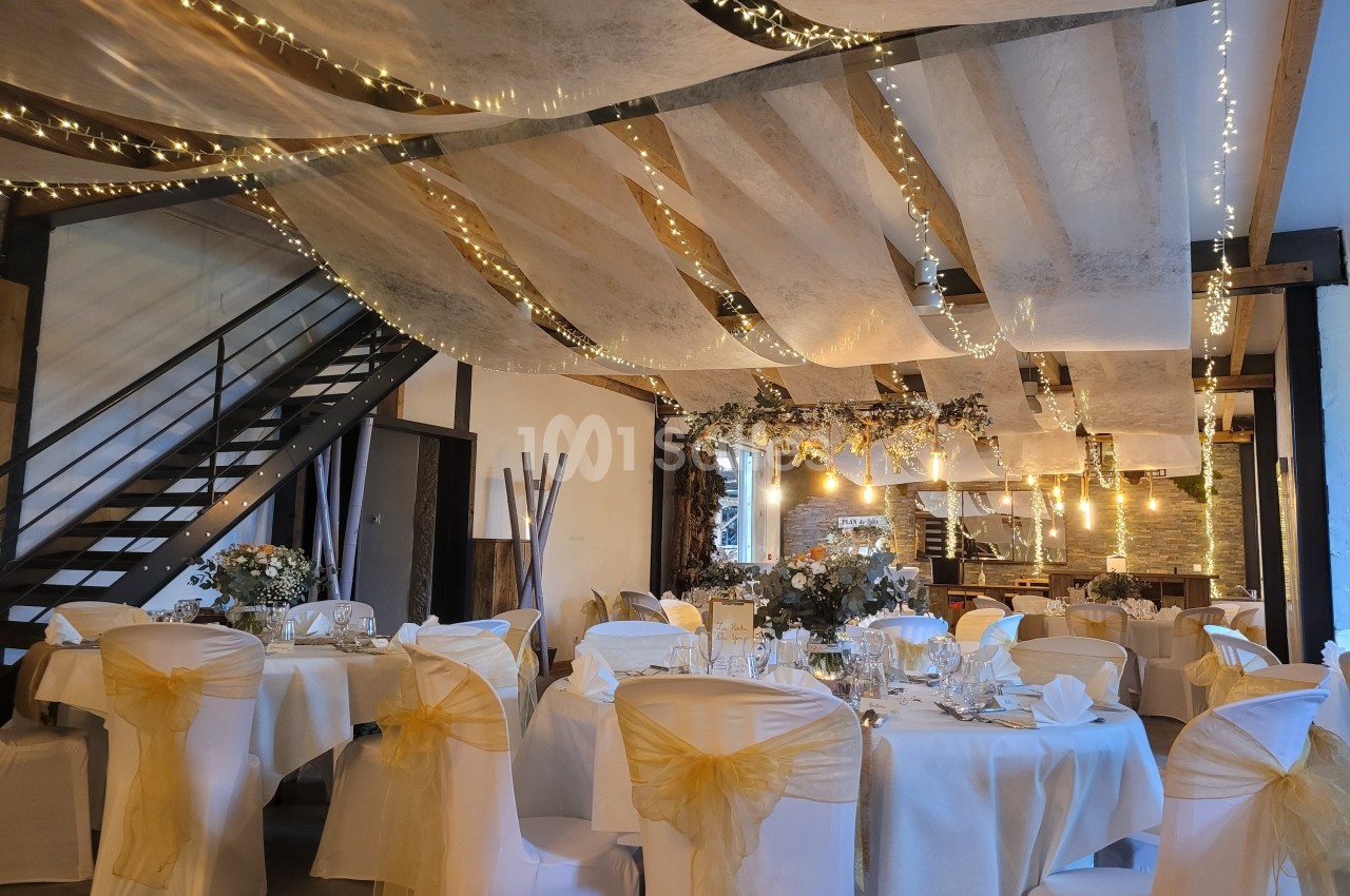 Salle de réception décorée avec des guirlandes lumineuses, des tables dressées et des chaises ornées de nœuds jaunes.