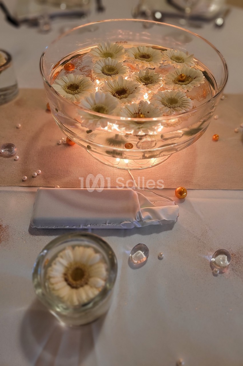 Bol en verre contenant des fleurs blanches flottantes, entouré de perles et décorations sur une table élégante.