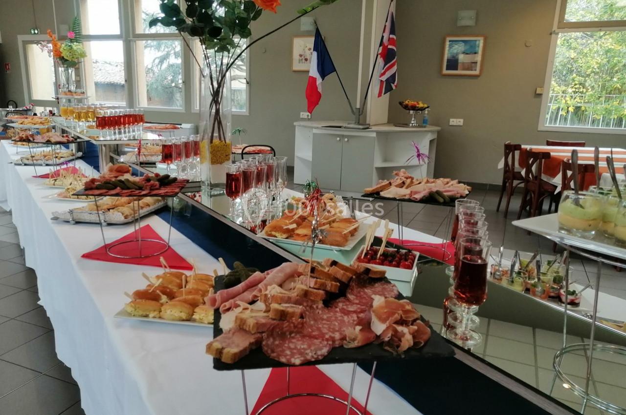 Buffet composé de charcuterie, verrines, toasts et boissons, disposé dans une salle lumineuse avec des drapeaux en arrière…