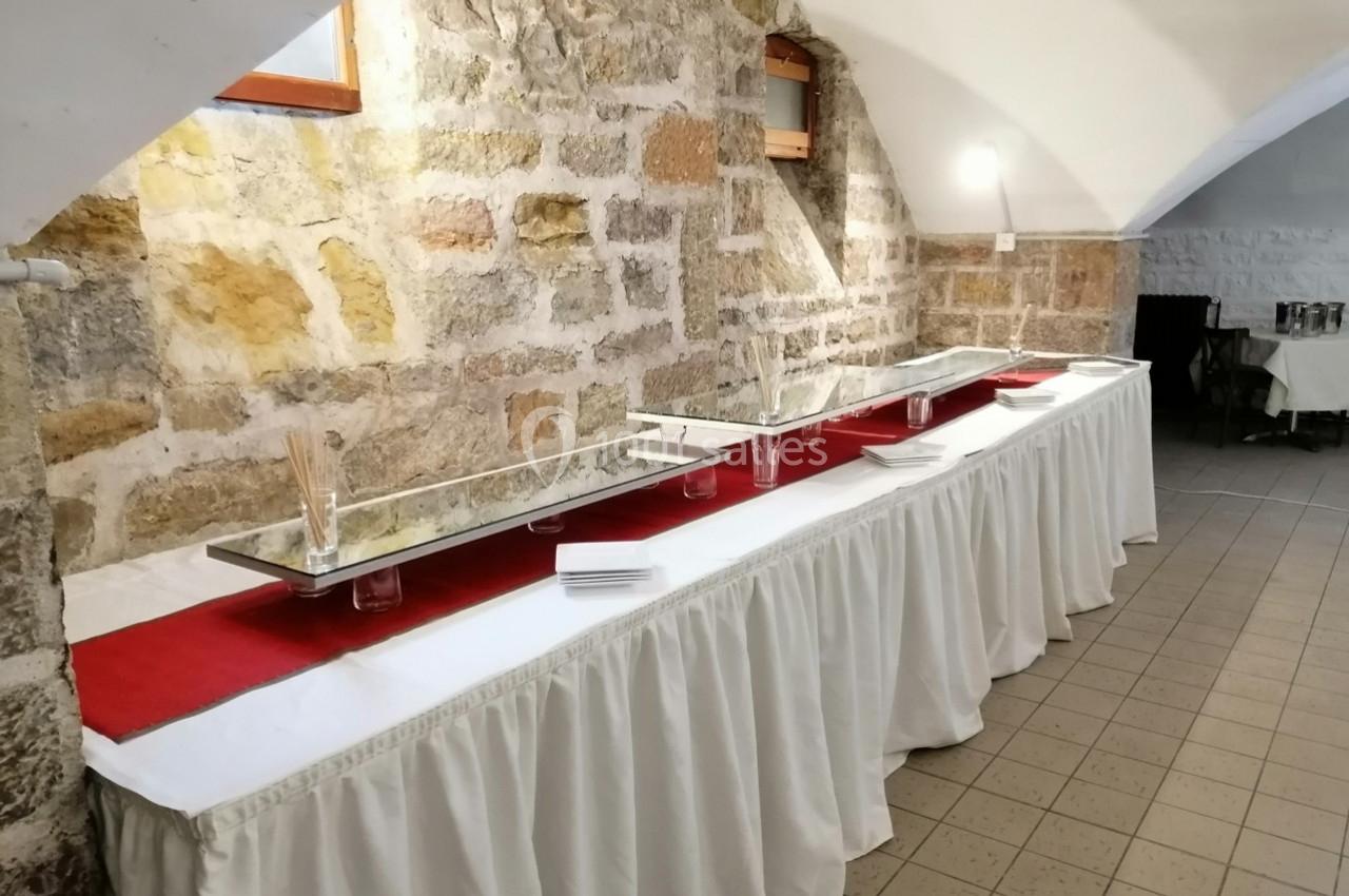 Table de buffet vide avec nappes blanches et chemins de table rouges, située dans une salle aux murs en pierre.
