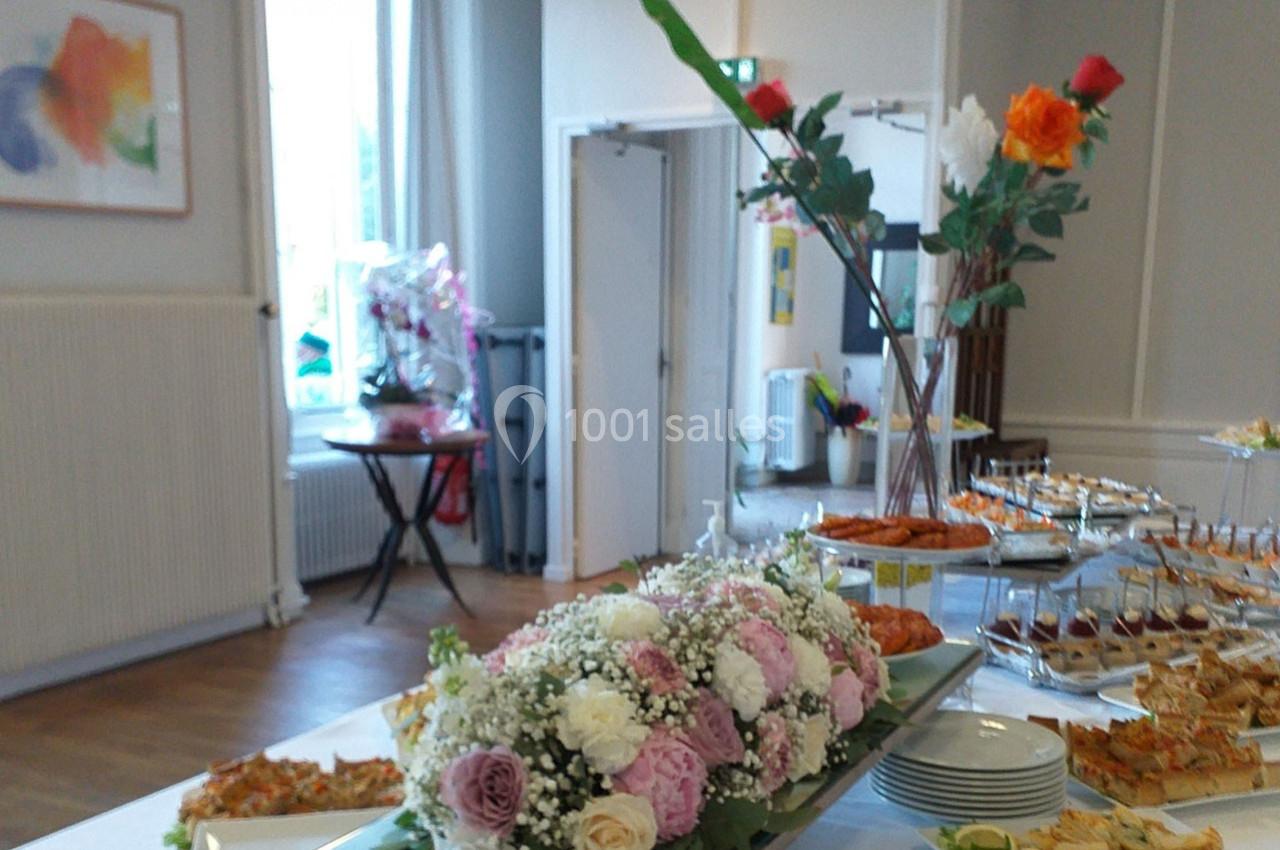 Buffet de réception avec fleurs en centre de table, assortiments de plats et décorations dans une salle lumineuse.