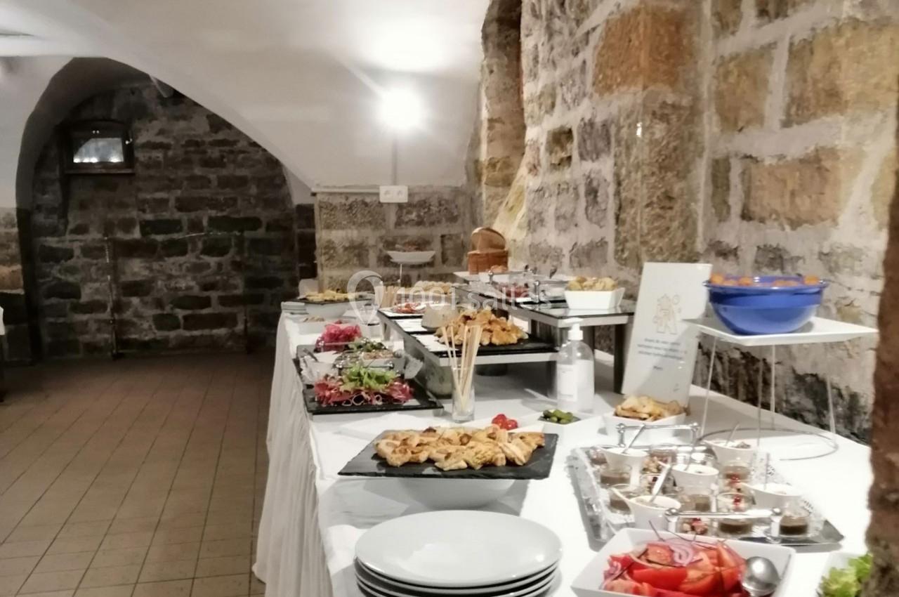 Buffet varié disposé sur des tables dans une salle voûtée en pierre, avec assiettes et plats prêts à être servis.