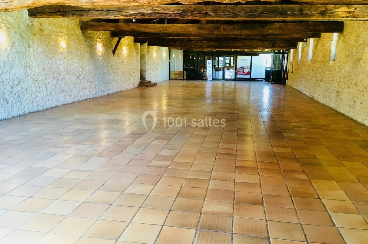 Salle spacieuse avec sol en carreaux de terre cuite, murs en pierre et poutres en bois apparentes.