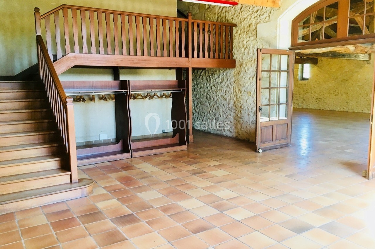 Salle spacieuse avec sol en carrelage, mezzanine en bois, murs en pierre et porte vitrée ouverte.