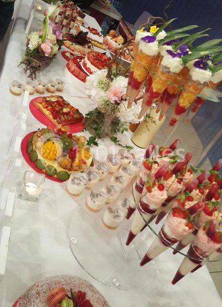 Table garnie de desserts variés, incluant verrines, fruits frais, pâtisseries et décorations florales.