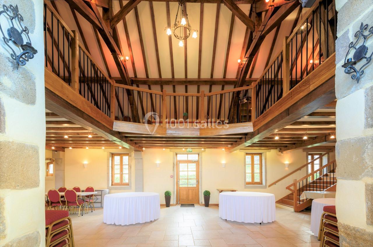 Salle lumineuse avec poutres apparentes, tables rondes dressées et chaises rouges, entourée de balustrades en bois.