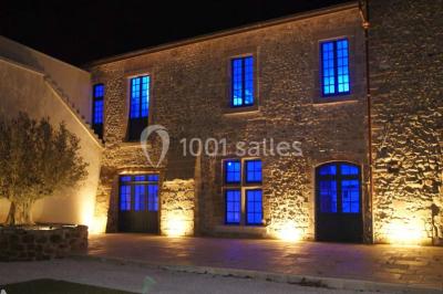 Allée éclairée par des lampes au sol, bordée d'arbres et menant à une entrée illuminée dans l'obscurité.