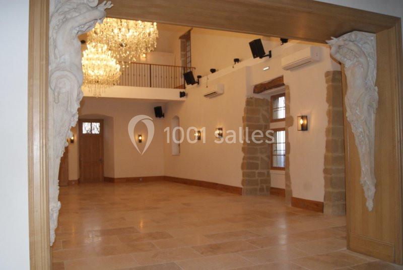 Salle lumineuse avec sol en pierre, lustres en cristal, moulures sculptées et murs ornés de pierres apparentes.