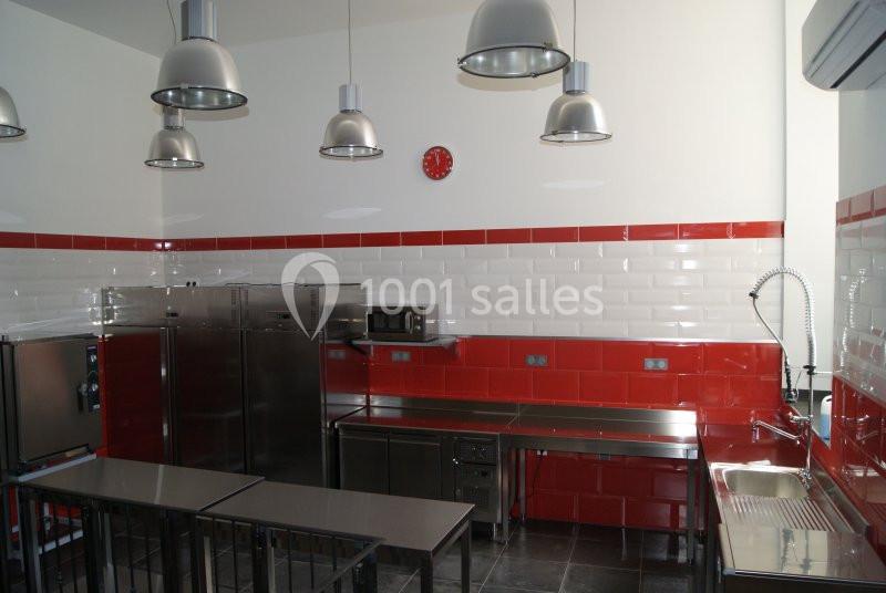 Cuisine professionnelle avec plans de travail en inox, murs carrelés rouge et blanc, et équipements industriels.