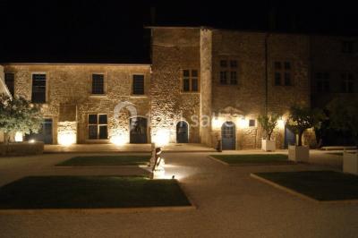Allée éclairée par des lampes au sol, bordée d'arbres et menant à une entrée illuminée dans l'obscurité.
