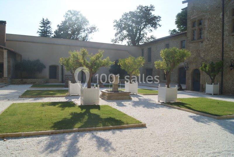 Cour intérieure avec fontaine centrale, arbres taillés, pelouses encadrées et bâtiments en pierre en arrière-plan.