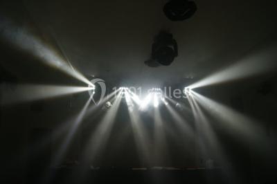 Allée éclairée par des lampes au sol, bordée d'arbres et menant à une entrée illuminée dans l'obscurité.