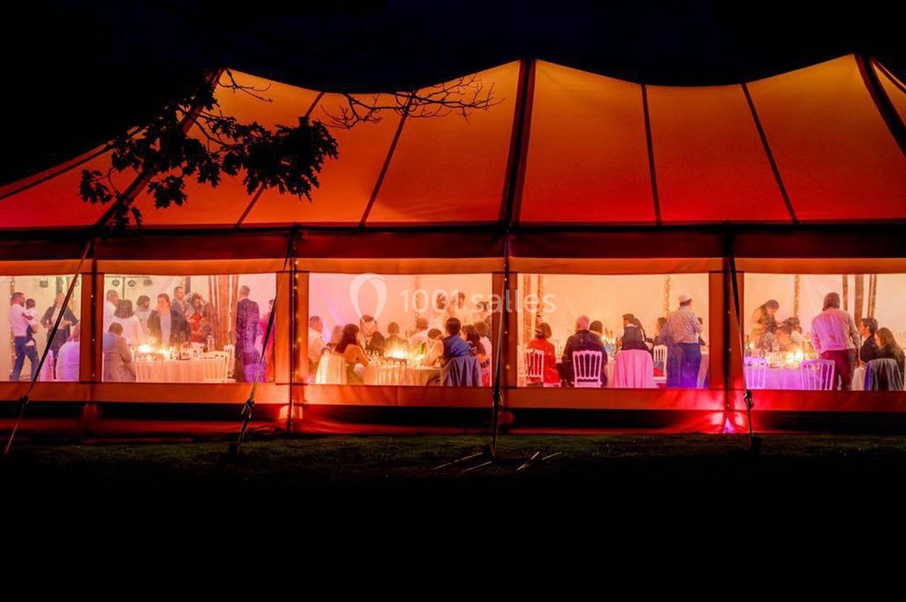 Tente éclairée en orange vif, abritant un dîner avec des convives assis autour de tables, vue de nuit.