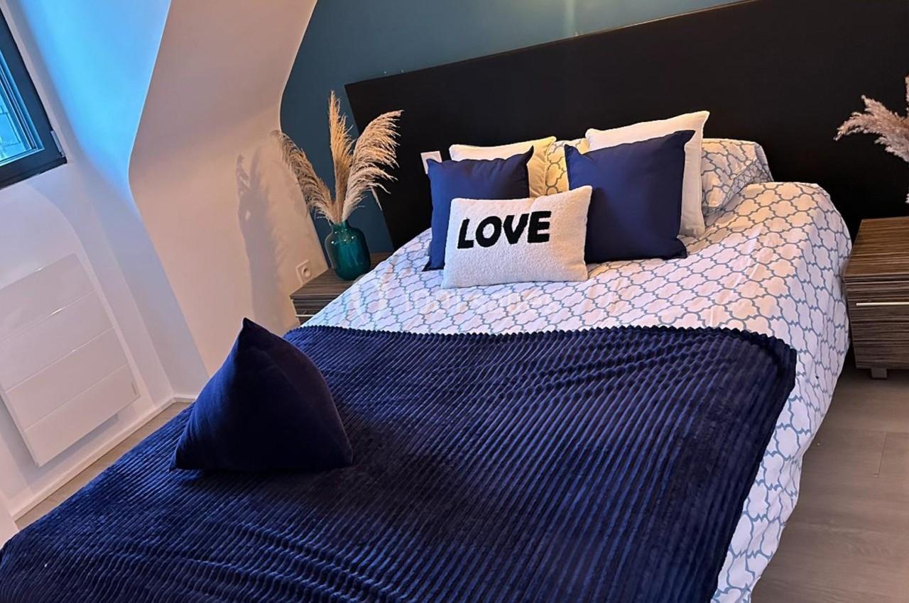 Lit double avec couvre-lit bleu, coussins décoratifs et vase de pampas, dans une chambre lumineuse au mur bleu.