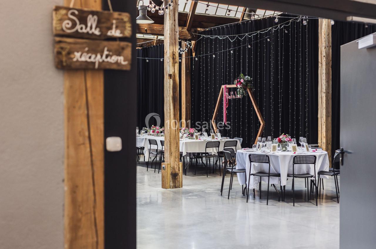 Salle de réception décorée avec des tables rondes dressées, des fleurs et des guirlandes lumineuses suspendues.