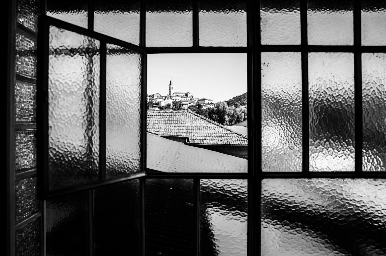Vue en noir et blanc d'un village avec un clocher, encadrée par une fenêtre à carreaux en verre dépoli.