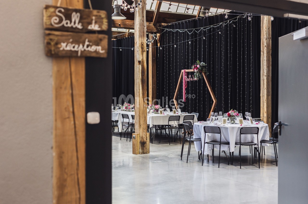 Salle de réception décorée avec des tables dressées, des fleurs et des guirlandes lumineuses suspendues.