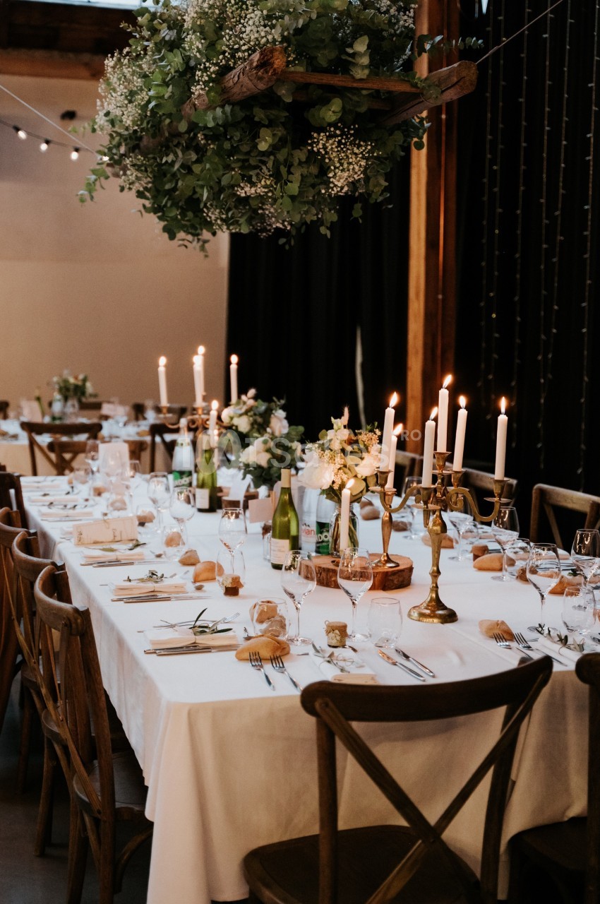 Table de réception élégamment dressée avec nappes blanches, chandeliers, fleurs et vaisselle raffinée.
