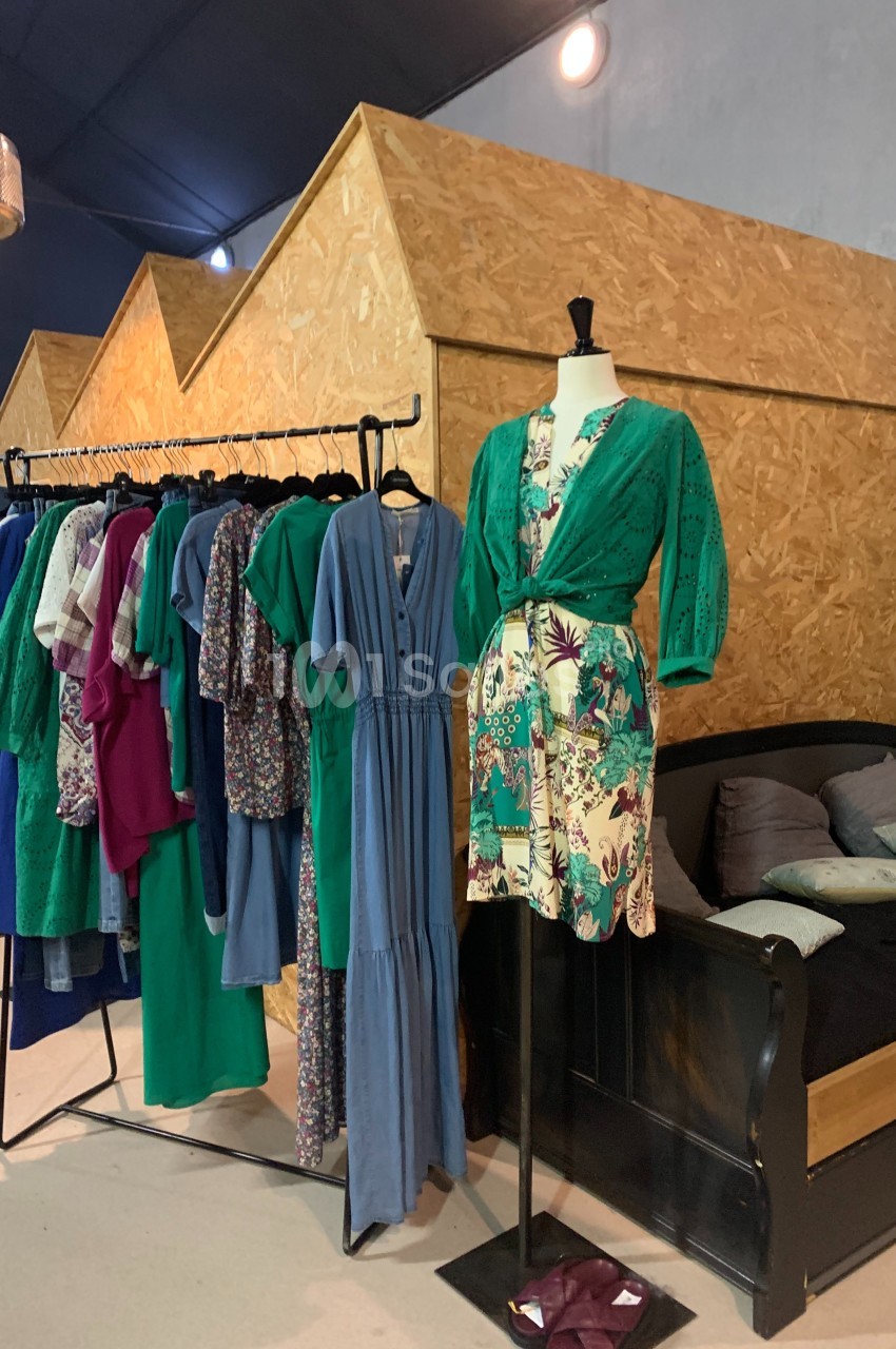 Portant de vêtements colorés à côté d'un mannequin habillé d'une robe verte et imprimée, dans un espace intérieur.