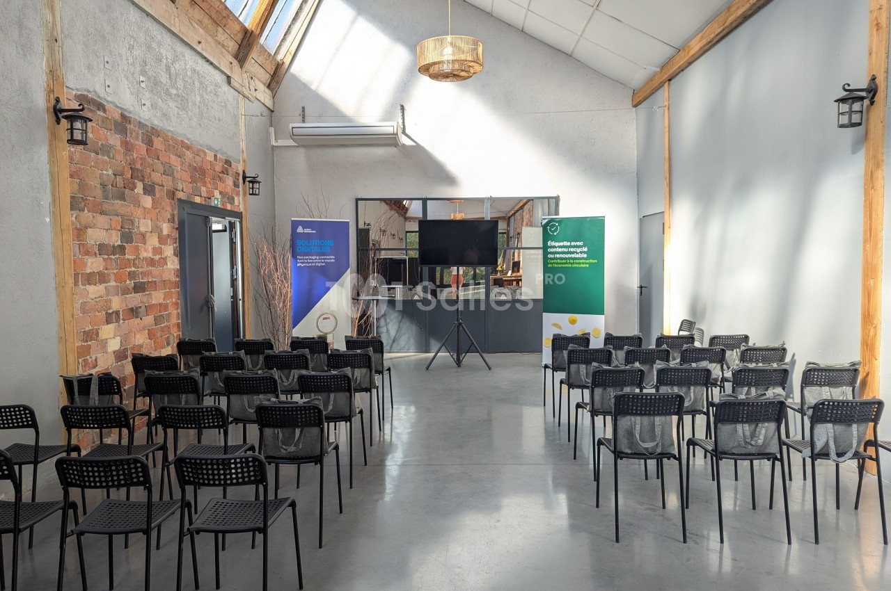 Salle lumineuse avec chaises noires alignées face à un écran et des panneaux d'information, murs en briques et bois.