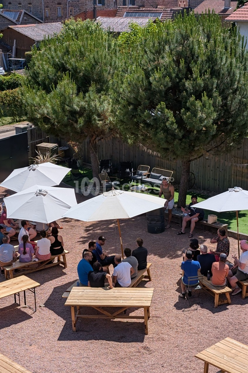 Groupe de personnes assises à des tables en extérieur sous des parasols, entourées d'arbres et de bâtiments.