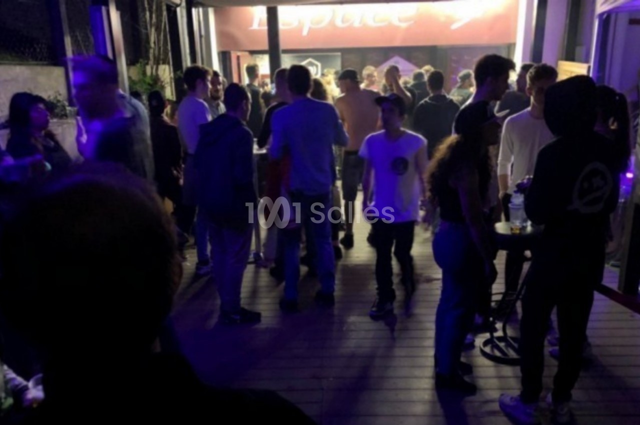 Groupe de personnes discutant et se déplaçant sur une terrasse éclairée par des lumières tamisées en soirée.