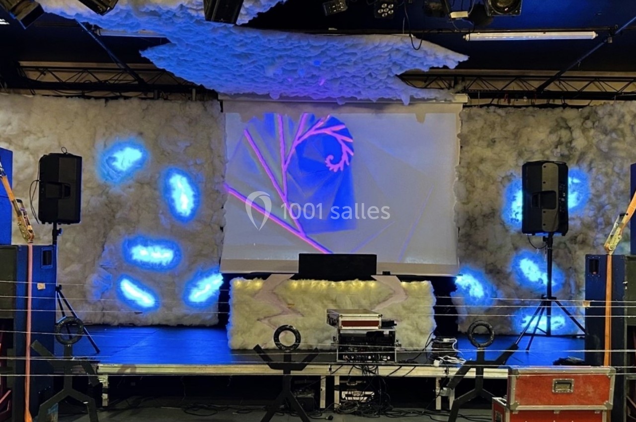 Scène décorée avec des éléments lumineux bleus, un écran projetant des motifs et des équipements audio.