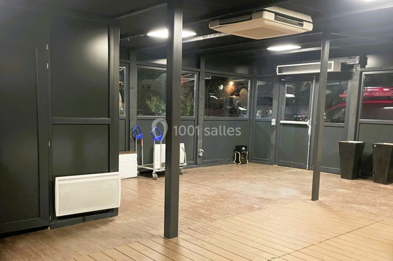 Salle vide avec murs sombres, parquet en bois, climatisation au plafond et fenêtres donnant sur l'extérieur.