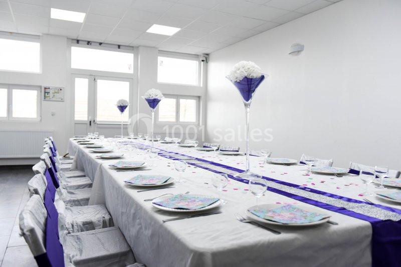 Table dressée pour un événement, décorée de nappes blanches, chemins de table violets et centres de table fleuris.