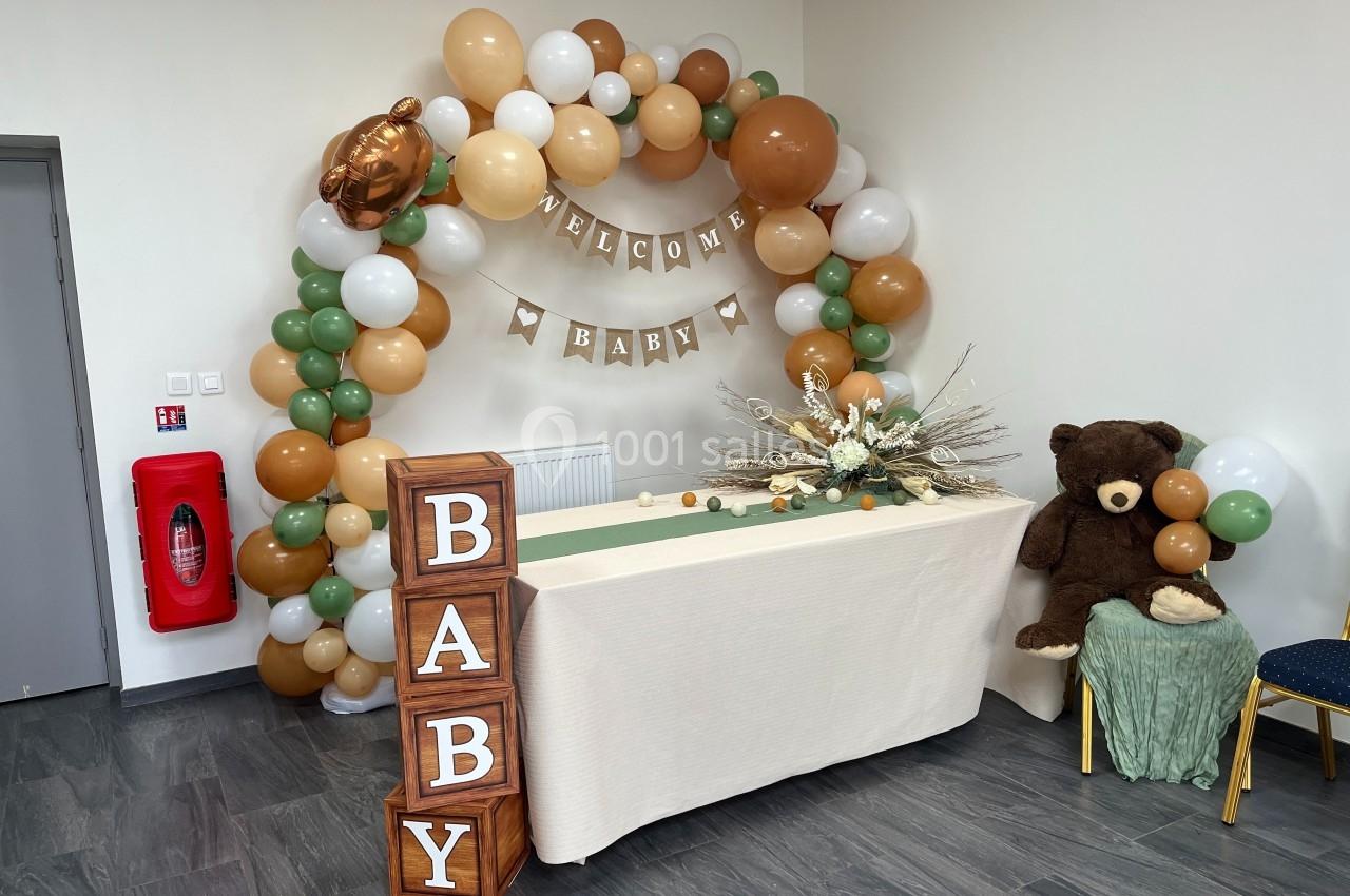 Décoration de fête avec arche de ballons beige et vert, table ornée de fleurs séchées et cubes formant le mot ’BABY’.