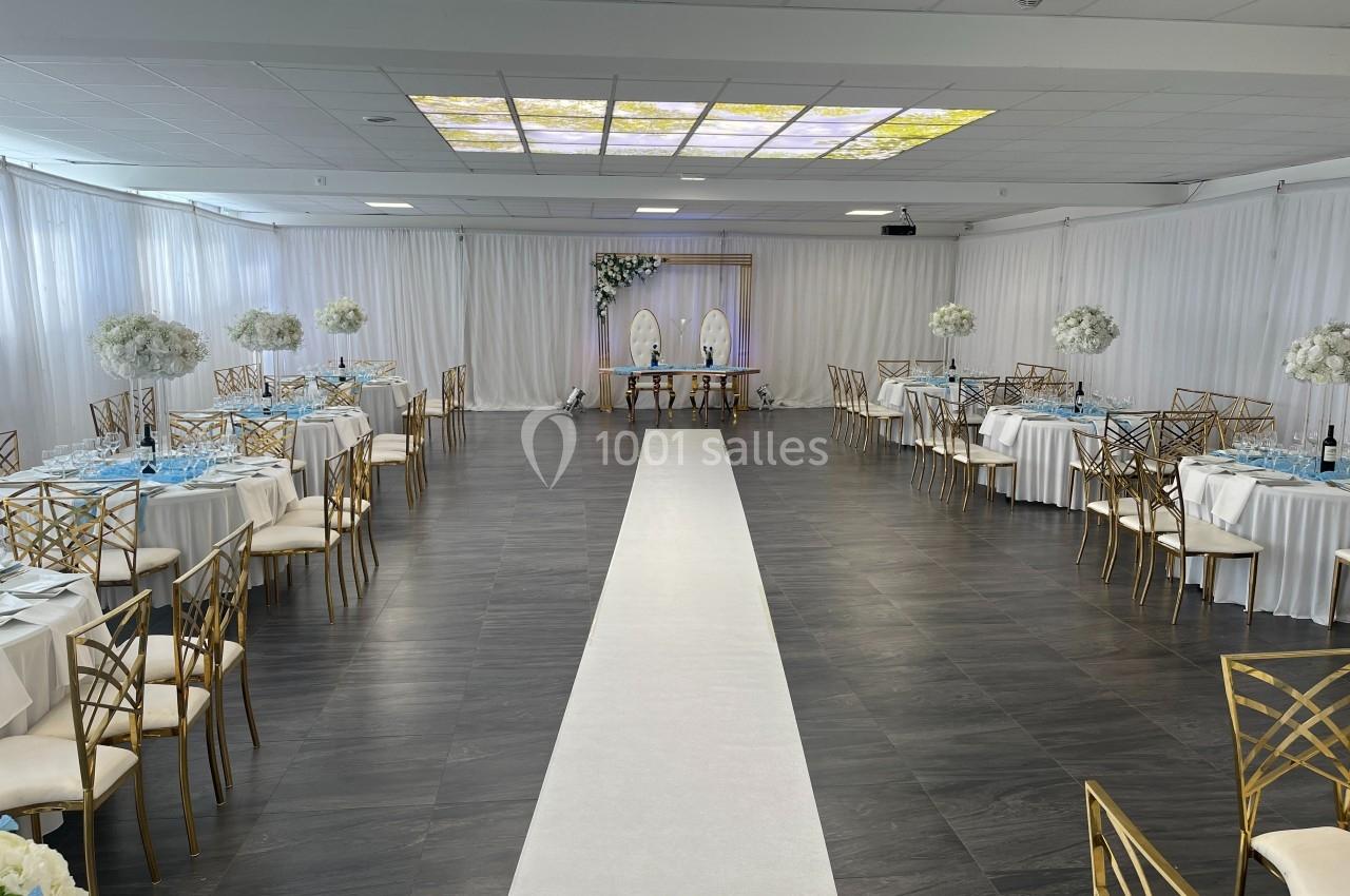 Salle de réception décorée avec des tables rondes, des chaises dorées et une allée centrale menant à une arche fleurie.