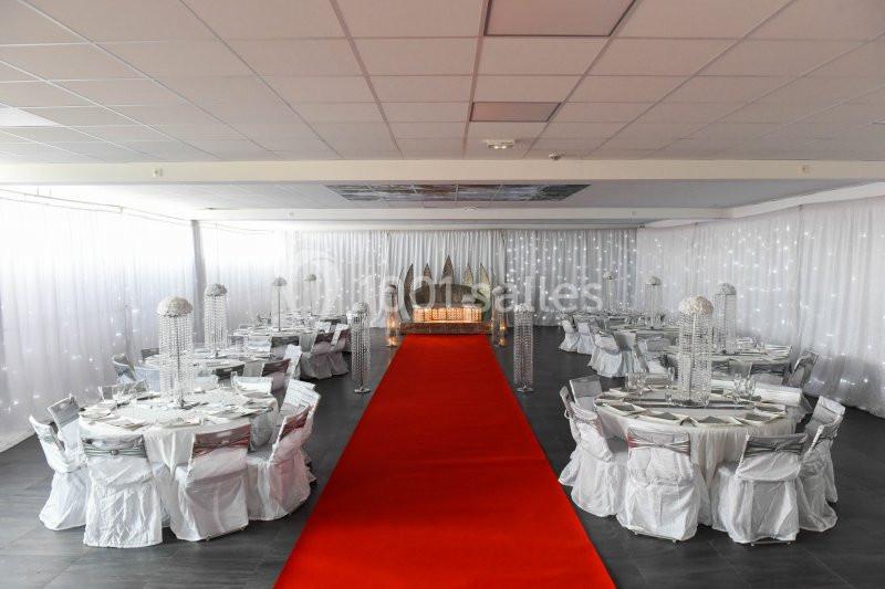 Location salle Hénin-Beaumont (Pas-de-Calais) - Team Square Events #8 Salle de réception décorée avec des tables rondes, chaises blanches et un tapis rouge menant à une estrade ornée.