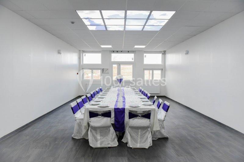 Location salle Hénin-Beaumont (Pas-de-Calais) - Team Square Events #10 Salle lumineuse avec une grande table rectangulaire dressée pour un repas, chaises décorées de housses blanches et rubans…