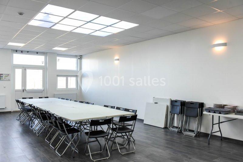 Location salle Hénin-Beaumont (Pas-de-Calais) - Team Square Events #9 Salle lumineuse avec grandes fenêtres, équipée d'une longue table entourée de chaises pliantes et d'un coin rangement.