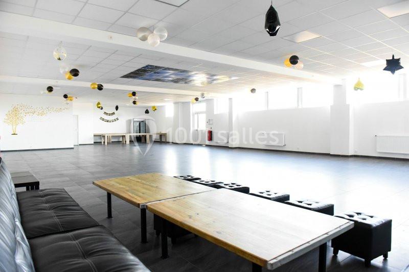 Salle spacieuse et lumineuse avec tables en bois, canapé noir, décorations suspendues et grandes fenêtres.