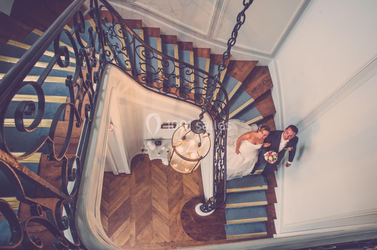 Vue plongeante sur un couple de mariés montant un escalier en colimaçon avec une rambarde en fer forgé.