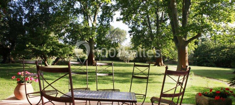 Mobilier de jardin en métal sur une terrasse en bois, avec vue sur un grand jardin verdoyant et des arbres.
