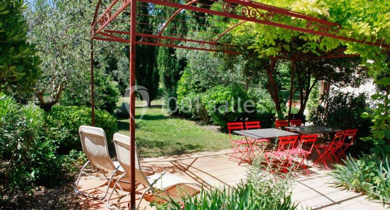 Terrasse ombragée avec pergola rouge, chaises longues et table entourée de chaises rouges dans un jardin verdoyant.