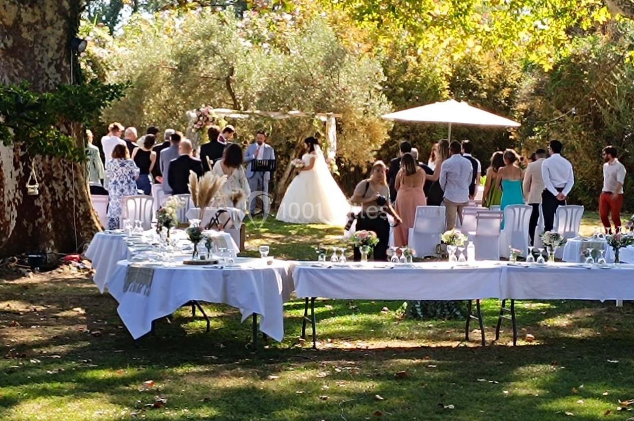 Cérémonie de mariage en plein air avec des invités rassemblés sous les arbres, tables dressées au premier plan.