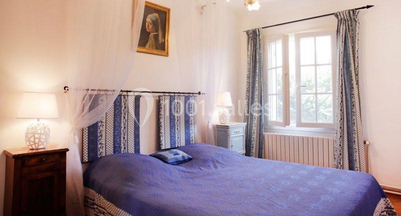 Chambre lumineuse avec lit double bleu, rideaux assortis, deux lampes de chevet et un tableau au mur.