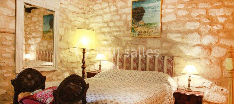 Chambre rustique avec murs en pierre, lit double, lampes de chevet et miroir encadré.