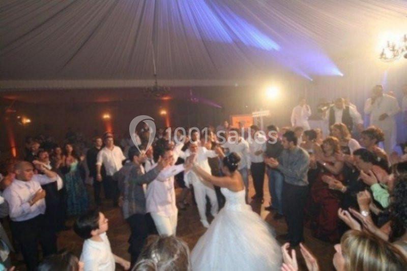 Des invités dansent autour d'une mariée en robe blanche dans une salle de réception éclairée.