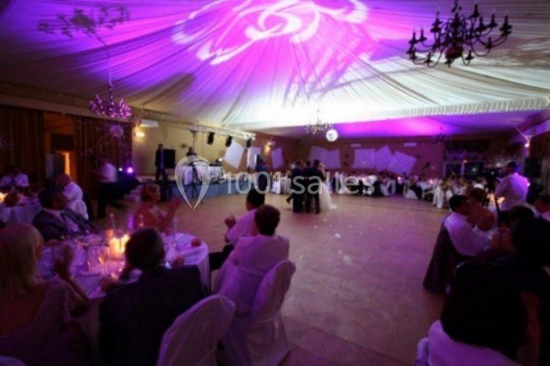 Salle de réception décorée avec un éclairage violet, des invités assis à des tables rondes et une piste de danse centrale.
