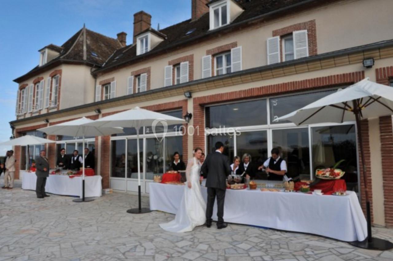 Mariage en extérieur devant une grande maison, avec des buffets sous parasols et des invités en tenue élégante.